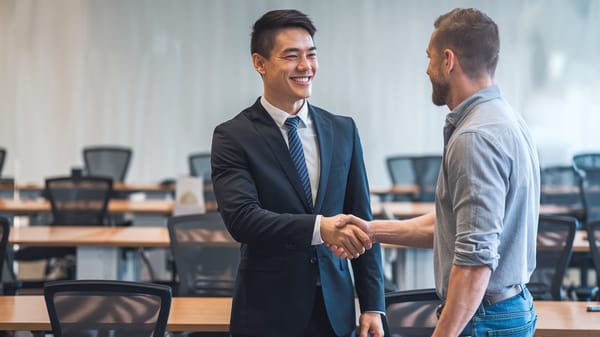 A business setting with a smiling Asian man and a Western man shaking hands.