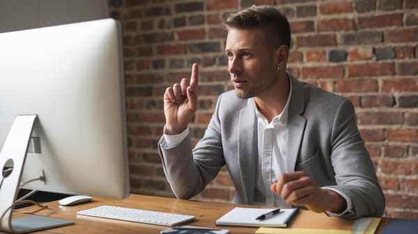 A cinematic shot of a marketing professional sitting at a desk. He is recording a video message. 