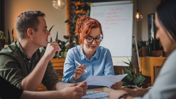 A photo of a collaborative planning team. There is a woman with red hair wearing glasses and a blue shirt. 