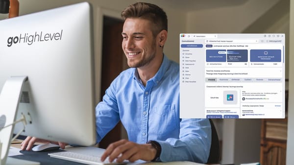 A photo of a man sitting at a desk, smiling as he works on his computer.