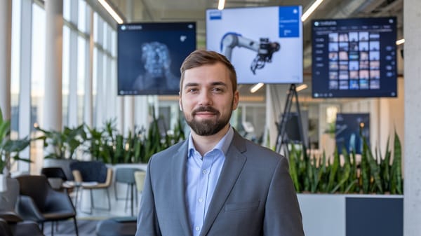 A photo of a man with a beard wearing a gray suit and a blue shirt.