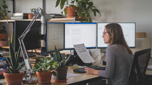 A photo of a woman sitting at a desk with multiple computer monitors. 