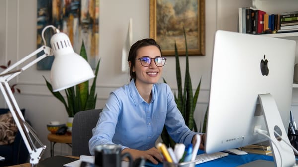 A photo of a woman wearing glasses and a blue shirt, sitting at a desk. 